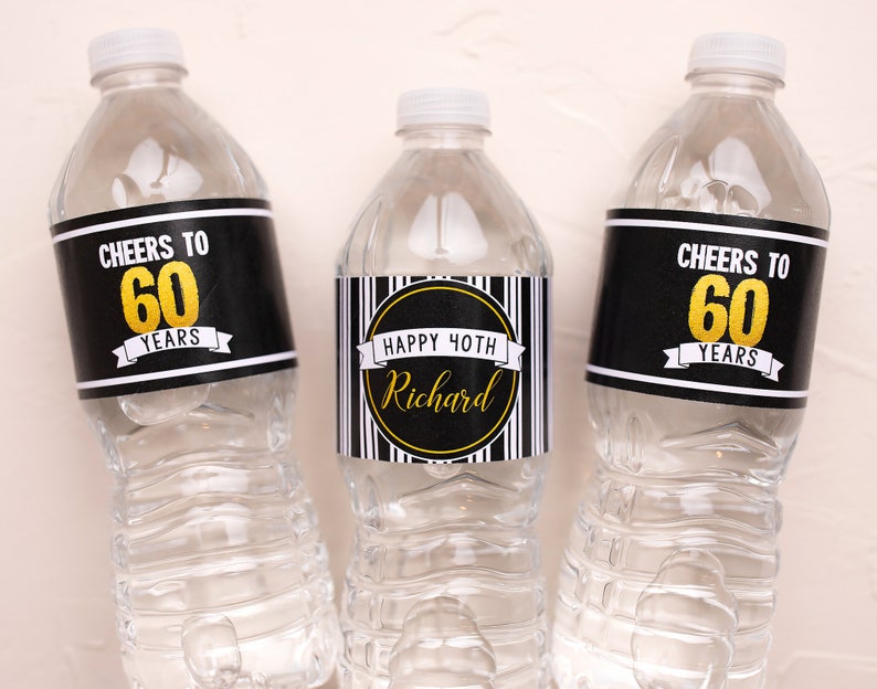 May include: Three clear plastic water bottles with custom labels. Two bottles have black labels with "Cheers to 60 Years" in white and gold. The centre bottle has a label that says "Happy 40th Richard".