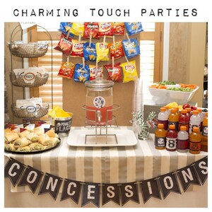 K&ouml;nnte beinhalten: Ein Tisch, der f&uuml;r eine Party mit einem Banner mit der Aufschrift "CONCESSIONS" gedeckt ist. Es gibt Snacks, Getr&auml;nke und Dekorationen mit Fu&szlig;ball-Thema. Der Tisch ist mit einer gestreiften Tischdecke bedeckt.