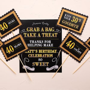 May include: Black and gold photo booth props with the text "40 Rocks", "40 Blows", "40 Sucks", "40 is Hot", "40 is Golden", and "Kiss Your 30's Goodbye". A black sign with white text reads "Grab a Bag Take a Treat Thanks for Helping Make Matt's Birthday Celebration So Sweet".