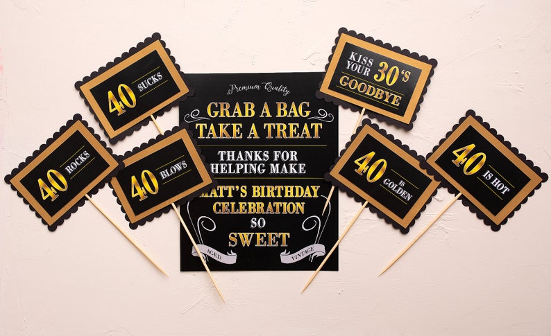 May include: Black and gold photo booth props with the text "40 Rocks", "40 Blows", "40 Sucks", "40 is Hot", "40 is Golden", and "Kiss Your 30's Goodbye". A black sign with white text reads "Grab a Bag Take a Treat Thanks for Helping Make Matt's Birthday Celebration So Sweet".