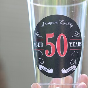 May include: A clear plastic cup with a black and white sticker that says "Premium Quality Aged 50 Years Vintage". The number 50 is in red.