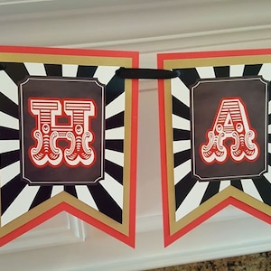 Op de afbeelding: Een rood, wit en zwart spandoek met het woord "Happy" in grote, rode, gestileerde letters. De letters zijn omlijst met zwart en goud.