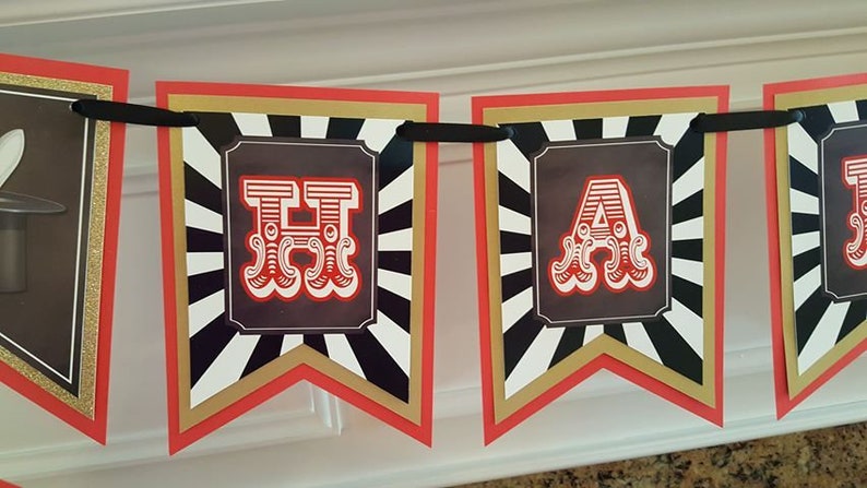 Op de afbeelding: Een rood, wit en zwart spandoek met het woord "Happy" in grote, rode, gestileerde letters. De letters zijn omlijst met zwart en goud.