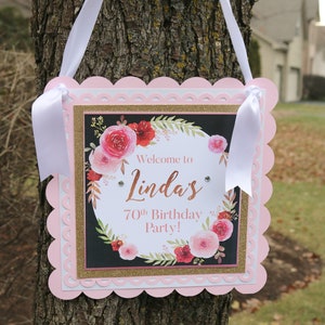 May include: Pink and gold welcome sign with a floral design and the text "Welcome to Linda's 70th Birthday Party!"
