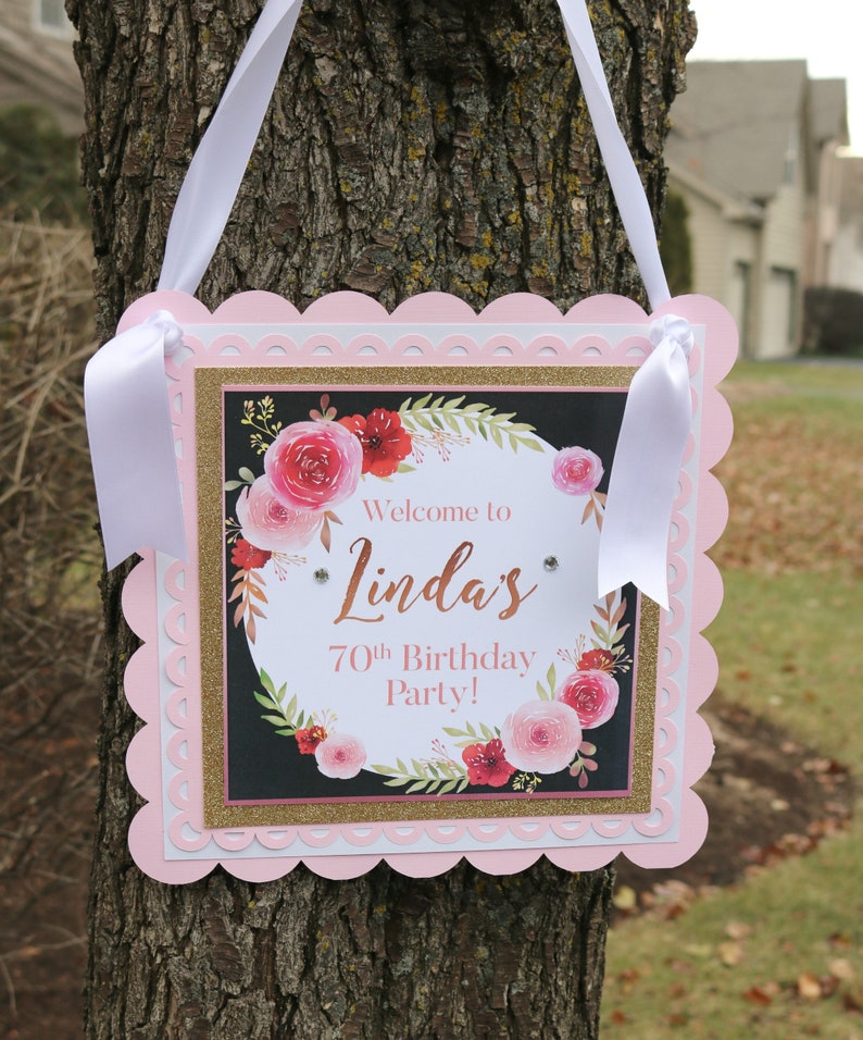 May include: Pink and gold welcome sign with a floral design and the text "Welcome to Linda's 70th Birthday Party!"