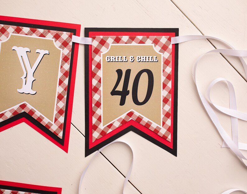 Peut inclure: Une guirlande avec les mots "Grill & Chill" et le chiffre "40" sur un fond beige. La guirlande a une bordure &agrave; carreaux rouges et blancs et est attach&eacute;e avec un ruban blanc. La guirlande est con&ccedil;ue pour une c&eacute;l&eacute;bration du 40e anniversaire.