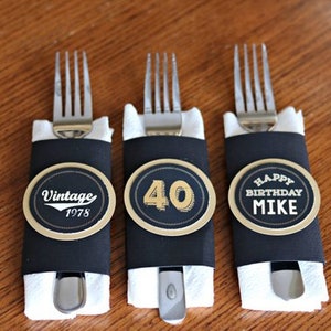 May include: Three black and gold party favor place card holders with forks wrapped in white napkins. The place cards say "Vintage 1978", "40", and "Happy Birthday Mike".