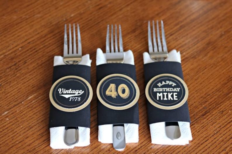 May include: Three black and gold party favor place card holders with forks wrapped in white napkins. The place cards say "Vintage 1978", "40", and "Happy Birthday Mike".