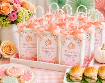 May include: A collection of white paper gift bags with handles, each featuring a peach-colored satin ribbon bow, a pumpkin illustration, and the printed text Thank You FOR CELEBRATING WITH US! Love Nora, arranged in a white rectangular tray.