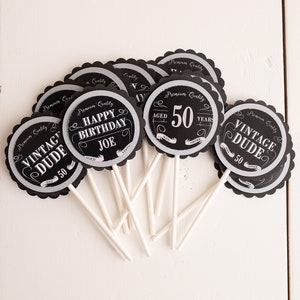 Puede incluir: Toppers para cupcakes en blanco y negro con un tema vintage. Los toppers presentan el texto "Vintage Dude" y "Happy Birthday Joe" con el n&uacute;mero 50.