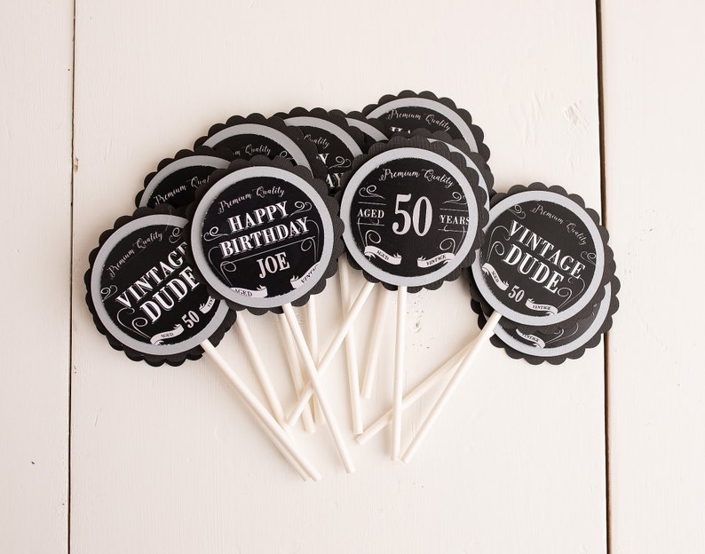 Puede incluir: Toppers para cupcakes en blanco y negro con un tema vintage. Los toppers presentan el texto "Vintage Dude" y "Happy Birthday Joe" con el n&uacute;mero 50.