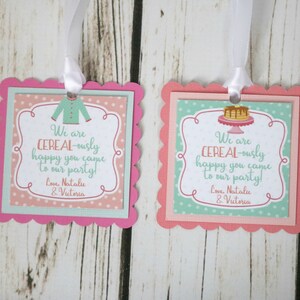 May include: Two pink and green favor tags with scalloped edges. The tags feature a cereal bowl with a spoon and a cereal box with a milk carton. The text on the tags reads "We are CEREAL-ously happy you came to our party! Love, Natalie & Victoria".