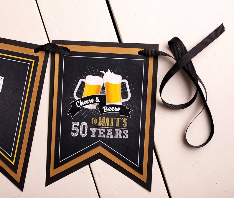Op de afbeelding: Een zwarte banner met gouden en witte accenten, met de tekst "Cheers & Beers to Matt's 50 Years" en illustraties van bierpullen. De banner is geregen met een zwart lint, perfect voor een mijlpaal verjaardag.