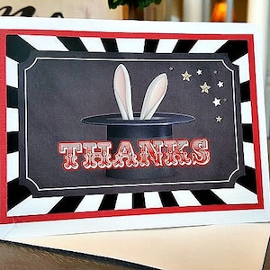 May include: A white card with a black and white striped border and a red stripe. The card has a black background with a white top hat and two white rabbit ears sticking out of the top. The text "THANKS" is in red letters with a white outline.