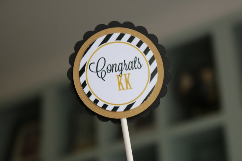 May include: Black and gold striped cupcake topper with the text "Congrats KK" in black script.