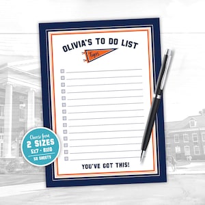 May include: A navy blue to-do list notepad with an orange and white border, and the text "OLIVIA'S TO DO LIST" at the top. A black pen rests on the notepad. The notepad includes the text "YOU'VE GOT THIS!"