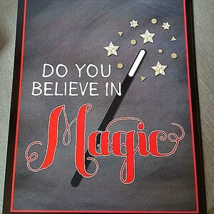 Pu&ograve; includere: Una lavagna nera con un bordo rosso e il testo "Credi nella magia?" scritto in bianco. Una bacchetta magica nera con stelle dorate &egrave; disegnata sulla lavagna.