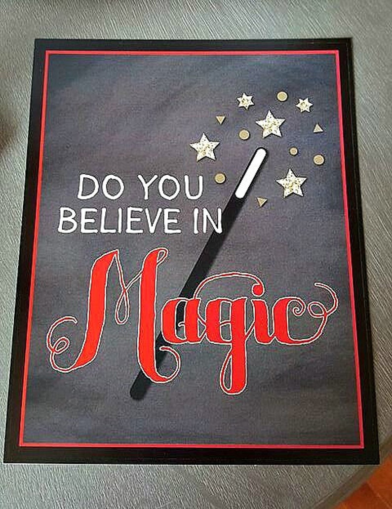 Pu&ograve; includere: Una lavagna nera con un bordo rosso e il testo "Credi nella magia?" scritto in bianco. Una bacchetta magica nera con stelle dorate &egrave; disegnata sulla lavagna.