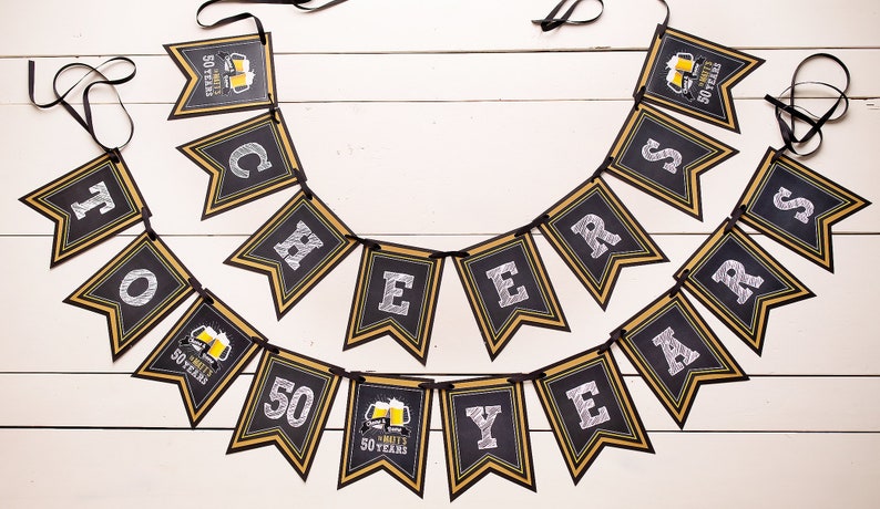 Op de afbeelding: Een zwart en goudkleurig spandoek met de tekst "Cheers to 50 Years". Elke vlag heeft een gouden rand en witte tekst. Sommige vlaggen hebben een biermok-afbeelding. De banner is geregen op een zwart lint.