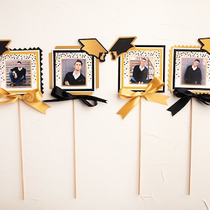 May include: Four graduation themed photo holders with black and gold confetti backgrounds. Each holder has a black graduation cap, a photo of a person, and a black or gold ribbon.