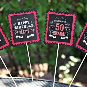 May include: Four black and red party signs with white text. The signs say "Aged 50 Years", "Happy Birthday Matt", "Cheers to 50 Years!" and "Vintage Dude 50".