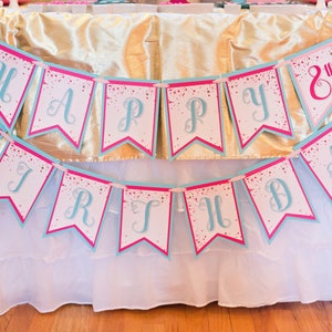 May include: A pink and blue banner with the words "Happy 8th Birthday" in a cursive font. The banner is decorated with white glitter.