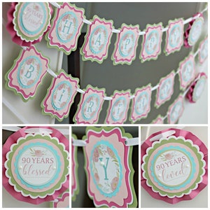 May include: A pink, green, and blue "Happy Birthday" banner with floral accents and the text "90 Years Blessed". The banner is strung with white ribbon and features scalloped edges.