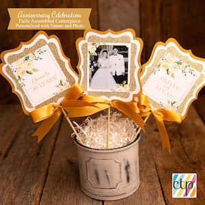 K&ouml;nnte beinhalten: Goldglitzer-Mittelst&uuml;ck mit einem Foto eines Paares, einem Schild mit der Aufschrift "Cheers to 50 Years!" und einem Schild mit der Aufschrift "Olivia und Lucas".