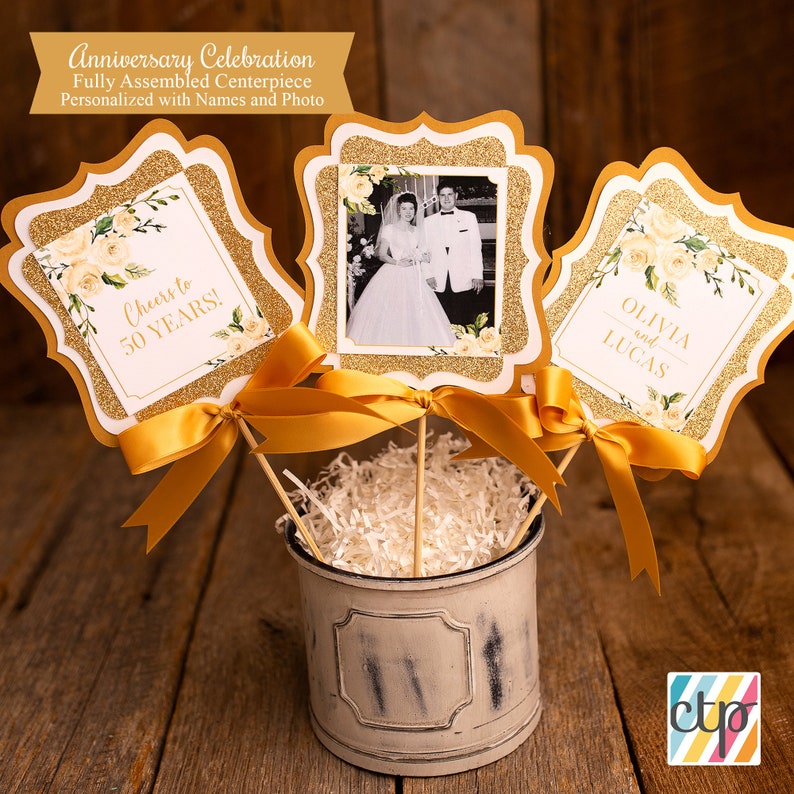 K&ouml;nnte beinhalten: Goldglitzer-Mittelst&uuml;ck mit einem Foto eines Paares, einem Schild mit der Aufschrift "Cheers to 50 Years!" und einem Schild mit der Aufschrift "Olivia und Lucas".