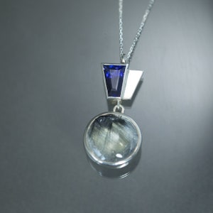 May include: A silver necklace with a round pendant featuring a clear stone with black streaks and a geometric silver and blue gemstone accent.