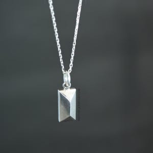 May include: A silver necklace with a geometric pendant. The pendant is a rectangular shape with a pointed top and bottom.