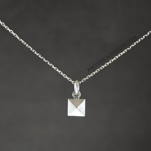May include: A silver chain necklace with a small, square pendant featuring a pyramid shape.