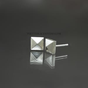 May include: A pair of silver pyramid-shaped stud earrings. The earrings are small and have a simple design.