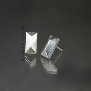 May include: A pair of silver geometric stud earrings. The earrings are rectangular in shape with a pointed top and bottom.