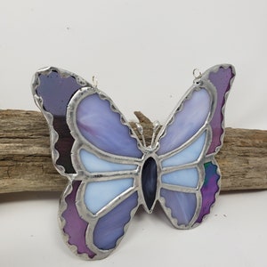 May include: A stained glass butterfly with purple, blue, and white glass pieces. The butterfly has a silver frame and is hanging from a silver wire.