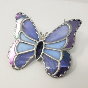 May include: A stained glass butterfly with iridescent purple, blue, and light blue glass pieces. The butterfly is outlined in silver metal.