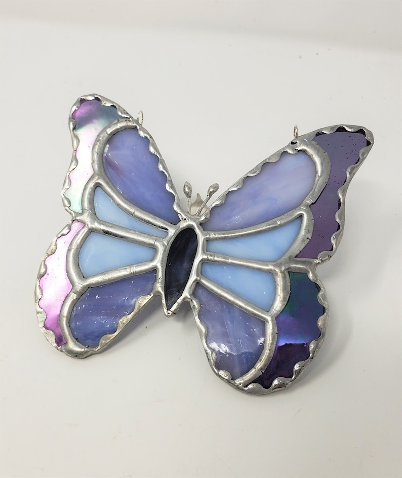 May include: A stained glass butterfly with iridescent purple, blue, and light blue glass pieces. The butterfly is outlined in silver metal.