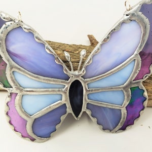 May include: A stained glass butterfly ornament with purple, pink, and blue glass pieces. The butterfly has a silver frame and is hanging from a silver wire.