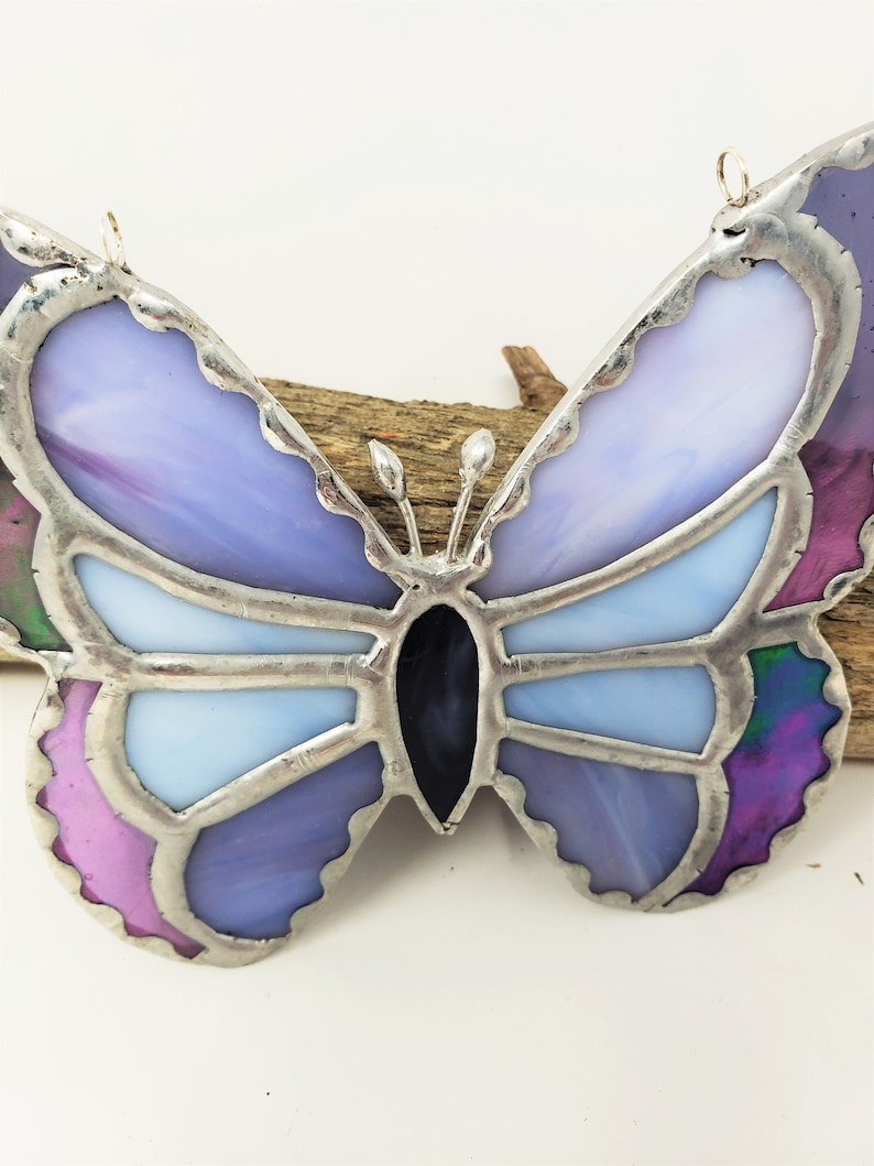 May include: A stained glass butterfly ornament with purple, pink, and blue glass pieces. The butterfly has a silver frame and is hanging from a silver wire.