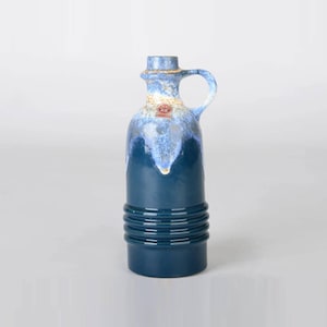 May include: A blue and white ceramic vase with a handle and a textured design. The vase has a blue glaze with white accents and a label on the side.