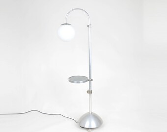 May include: A silver floor lamp with a white globe shade and a small round shelf. The lamp has a curved arm and a round base.