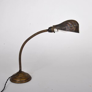 Peut inclure: Une lampe de bureau vintage en laiton avec un bras flexible en col de cygne et un abat-jour en métal nervuré. La lampe a un design simple et industriel.