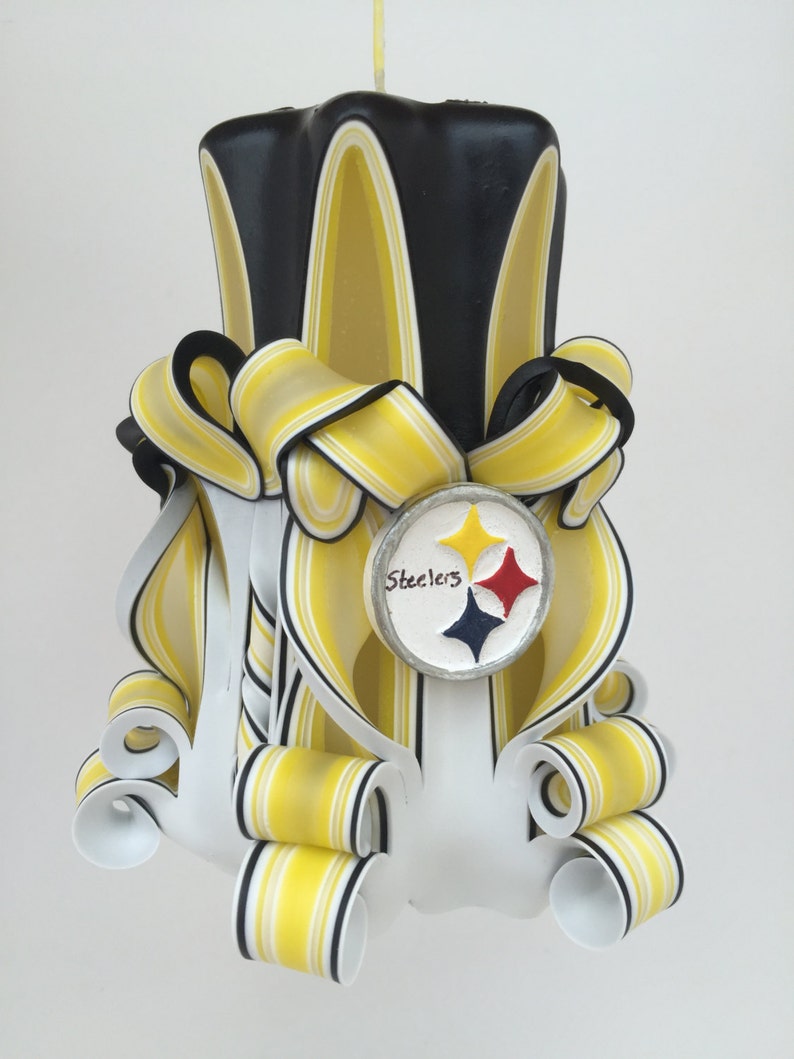 May include: A hand-crafted candle in black, white and yellow with a Steelers logo. The candle is decorated with yellow and black stripes and has a white base.