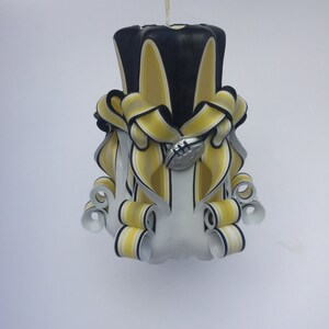 May include: A white, black and yellow striped candle with a football design. The candle is decorated with black and yellow ribbons.