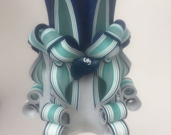 May include: A blue and green striped candle with a decorative swirl design. The candle is made of wax and has a white wick.
