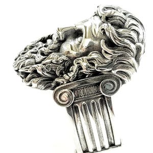 A large silver ring featuring the powerful figure of Zeus, the king of the gods, intricately carved atop a sturdy band.  Flanked by majestic Greek columns on each side, this bold statement piece exudes strength, sophistication, and timeless appeal.