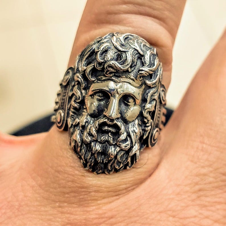 Silver Zeus ring on man's finger showing the Greek God's face enface