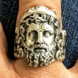 A silver Poseidon ring on a man's finger with the shank decorated with his trident