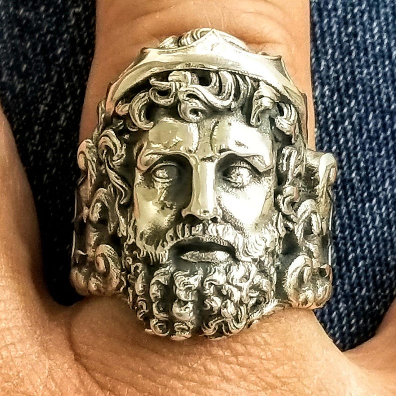 A silver Poseidon ring on a man's finger with the shank decorated with his trident