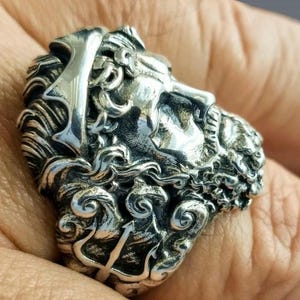 A silver Poseidon ring on a man's finger with the shank decorated with his trident
